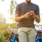 Choosing Bicycle - man holding smartphone leaning on bicycle during daytime