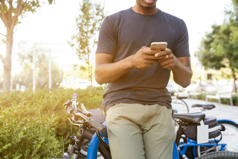 Choosing Bicycle - man holding smartphone leaning on bicycle during daytime