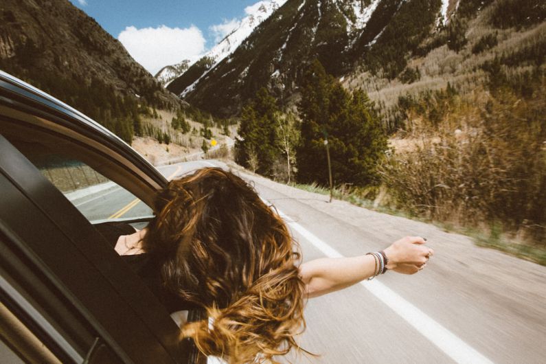 Travel Safety - woman riding on vehicle putting her head and right arm outside the window while travelling the road