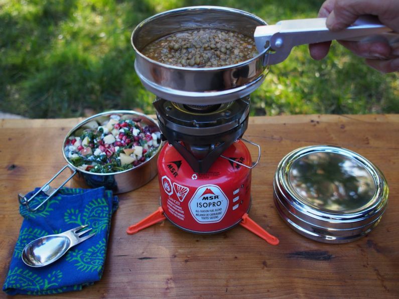 Eco-friendly Camping - person holding pot on red single burner top on brown wooden table