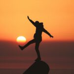 Balancing Life - photo of silhouette photo of man standing on rock