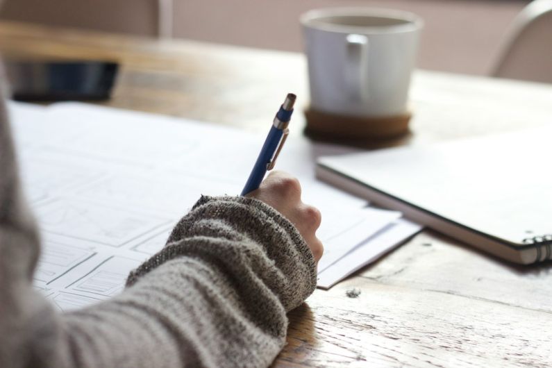Writing Resume - person writing on brown wooden table near white ceramic mug